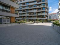 a group of buildings on an outside plaza with people on bicycles and skateboards parked