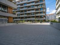 a group of buildings on an outside plaza with people on bicycles and skateboards parked