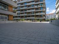 a group of buildings on an outside plaza with people on bicycles and skateboards parked