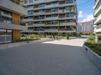 a group of buildings on an outside plaza with people on bicycles and skateboards parked