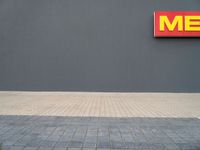 a yellow fire hydrant standing next to a gray wall with a me sign above it