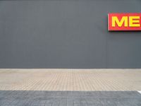 a yellow fire hydrant standing next to a gray wall with a me sign above it