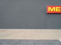 a yellow fire hydrant standing next to a gray wall with a me sign above it