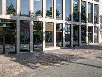 people walking in front of a building with glass windows with sun shining in the reflection