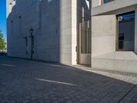 two people walking down an empty city street in an alley area with tall buildings in the background