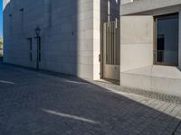 two people walking down an empty city street in an alley area with tall buildings in the background