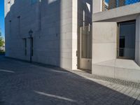 two people walking down an empty city street in an alley area with tall buildings in the background