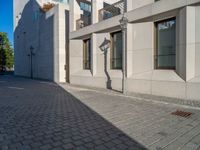 two people walking down an empty city street in an alley area with tall buildings in the background