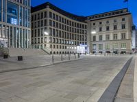 a wide city street with some buildings lit up at night behind it and the steps leading up to it are lined with empty benches