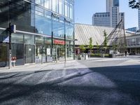 a glass and steel building on the corner with cobblestone on the side of the street