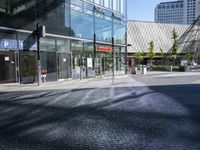 a glass and steel building on the corner with cobblestone on the side of the street