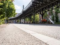 a person is riding a skate board down a sidewalk under a bridge on a sunny day