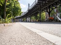 a person is riding a skate board down a sidewalk under a bridge on a sunny day