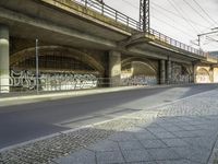 there is a long empty road under a bridge with graffiti on it and a sidewalk and building in the background