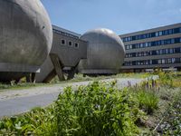 three large metallic spheres in front of a building in a city with tall buildings and bushes on the side