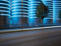 blue neon lights on the wall and road of an urban building, lit by a light in front of a tree