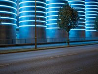 blue neon lights on the wall and road of an urban building, lit by a light in front of a tree