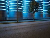 blue neon lights on the wall and road of an urban building, lit by a light in front of a tree