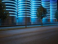 blue neon lights on the wall and road of an urban building, lit by a light in front of a tree