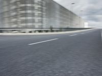 a blurred photo of a bike moving down a street with buildings in the background and a large building on one side