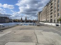 the walkway is empty in the city and is overlooking the river below it are buildings and cars