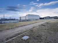 a grassy field in front of some white buildings on a blue cloudy day in summer