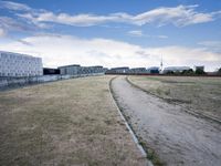 a grassy field in front of some white buildings on a blue cloudy day in summer