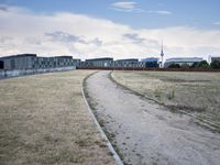 a grassy field in front of some white buildings on a blue cloudy day in summer
