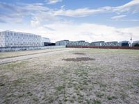 a grassy field in front of some white buildings on a blue cloudy day in summer
