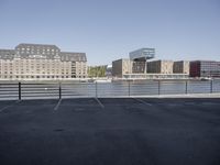 empty parking lot on the river with many buildings in the background behind it and another is visible on a blue sky day