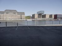 empty parking lot on the river with many buildings in the background behind it and another is visible on a blue sky day