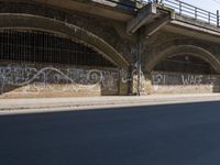 graffiti covered brick wall and gate under an overpass in an urban area with sun light