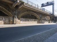 graffiti covered brick wall and gate under an overpass in an urban area with sun light
