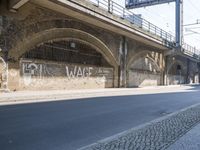 graffiti covered brick wall and gate under an overpass in an urban area with sun light