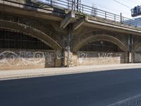 graffiti covered brick wall and gate under an overpass in an urban area with sun light