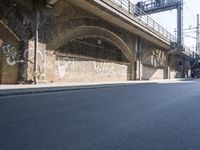 graffiti covered brick wall and gate under an overpass in an urban area with sun light
