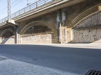graffiti covered brick wall and gate under an overpass in an urban area with sun light