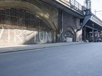 graffiti covered brick wall and gate under an overpass in an urban area with sun light