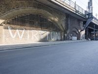 graffiti covered brick wall and gate under an overpass in an urban area with sun light