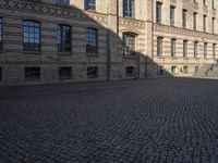 a person riding a bicycle in an empty street area with buildings and cobblestones