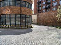 a curved building sits in the middle of a cobblestone parking lot with several tall buildings