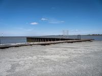 an old dock with water and a large body of water behind it and a sky filled with clouds