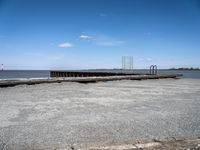 an old dock with water and a large body of water behind it and a sky filled with clouds