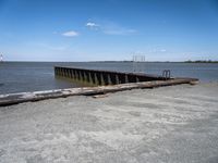 an old dock with water and a large body of water behind it and a sky filled with clouds