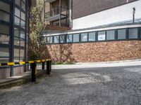 yellow and black barriers line a brick walk way outside an empty building with a brick wall behind