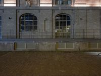 an empty street next to a brick building at night with a clock on it's face