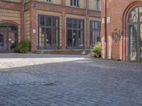 a brick courtyard outside of a large building with an archway at the end of it