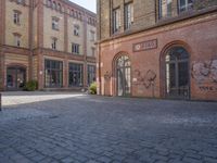 a brick courtyard outside of a large building with an archway at the end of it