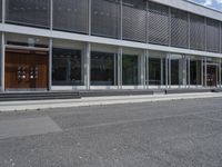 two people walking down the side walk towards a modern building with a large open glass front entrance