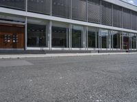 two people walking down the side walk towards a modern building with a large open glass front entrance